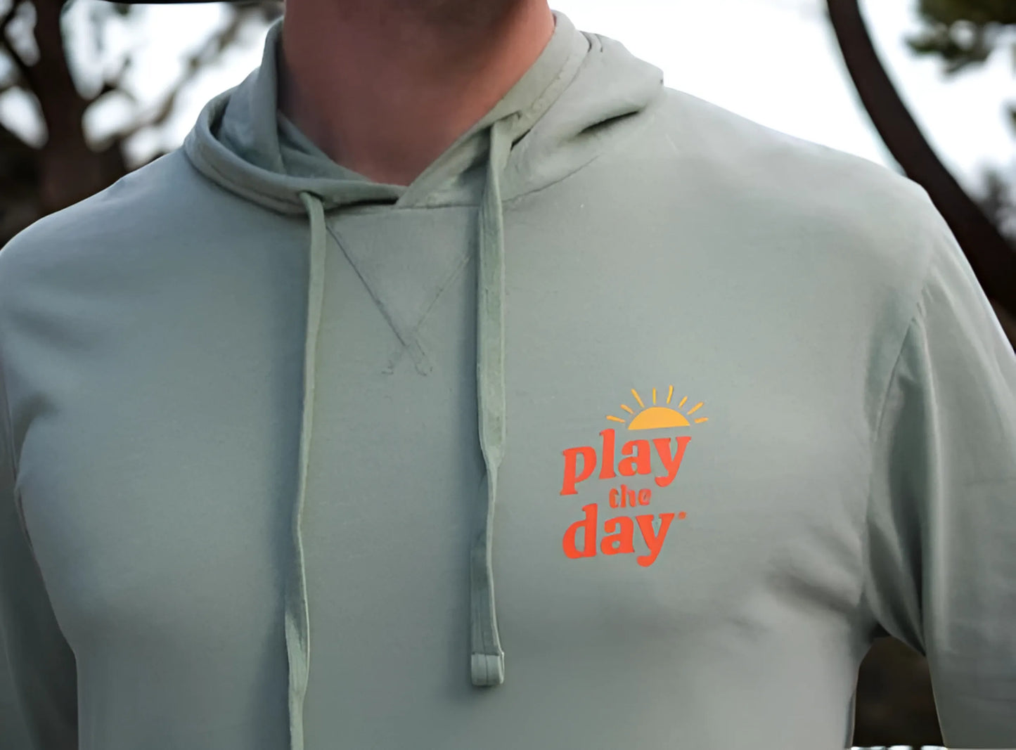 Light green hoodie with 'play the day' text on a blurred outdoor background