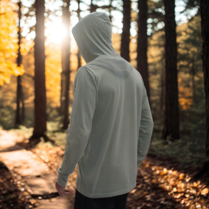 Person wearing a light green Play the Day hoodie walking through a forest with autumn foliage.