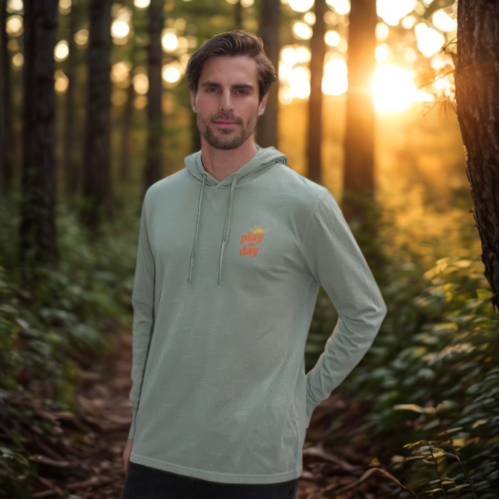 Man wearing a light green hoodie with a logo in a forest during sunset