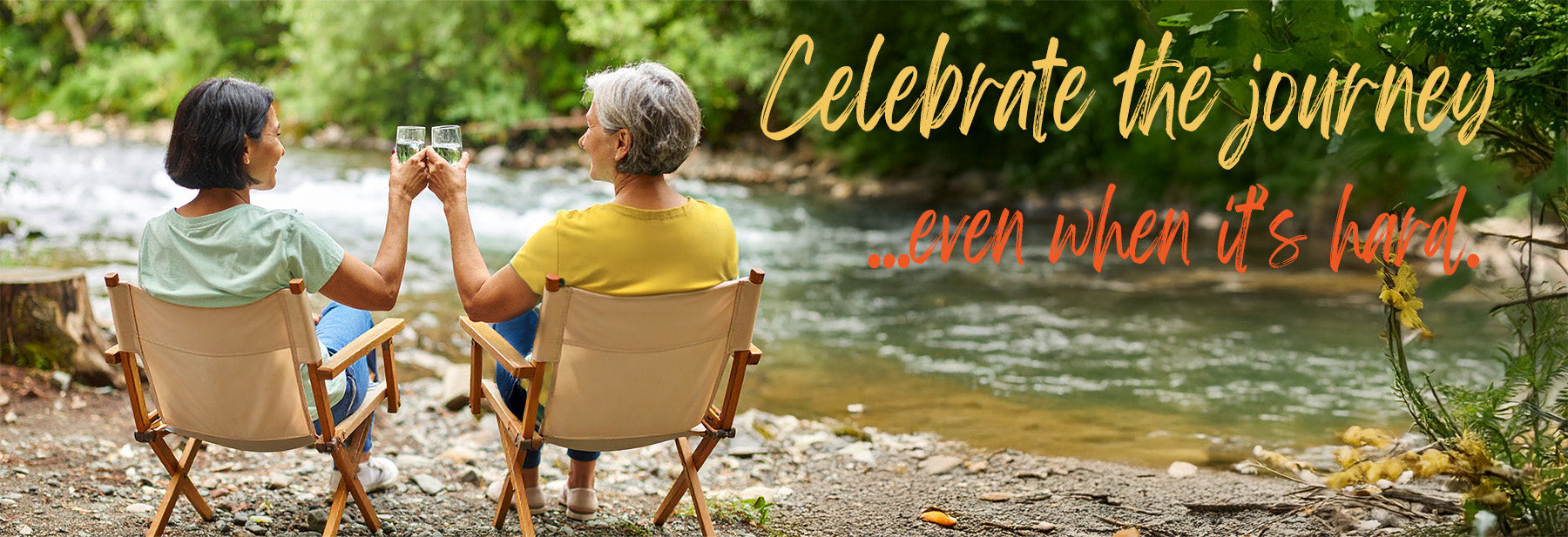 Two women clinking glasses in camping chairs beside a river with the quote ‘Celebrate the journey... even when it’s hard.'