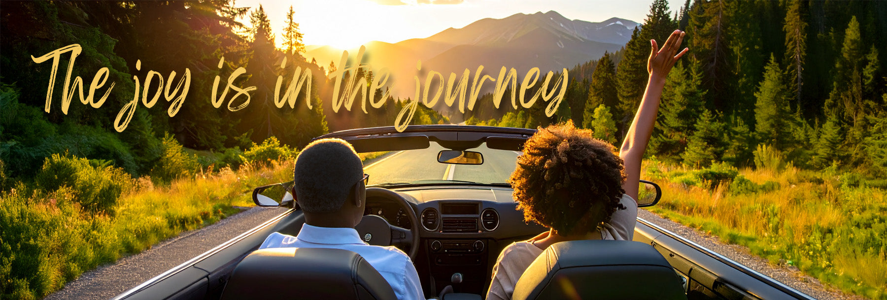 Couple driving into the sunset through a mountain forest in a convertible with the quote ‘The joy is in the journey.’