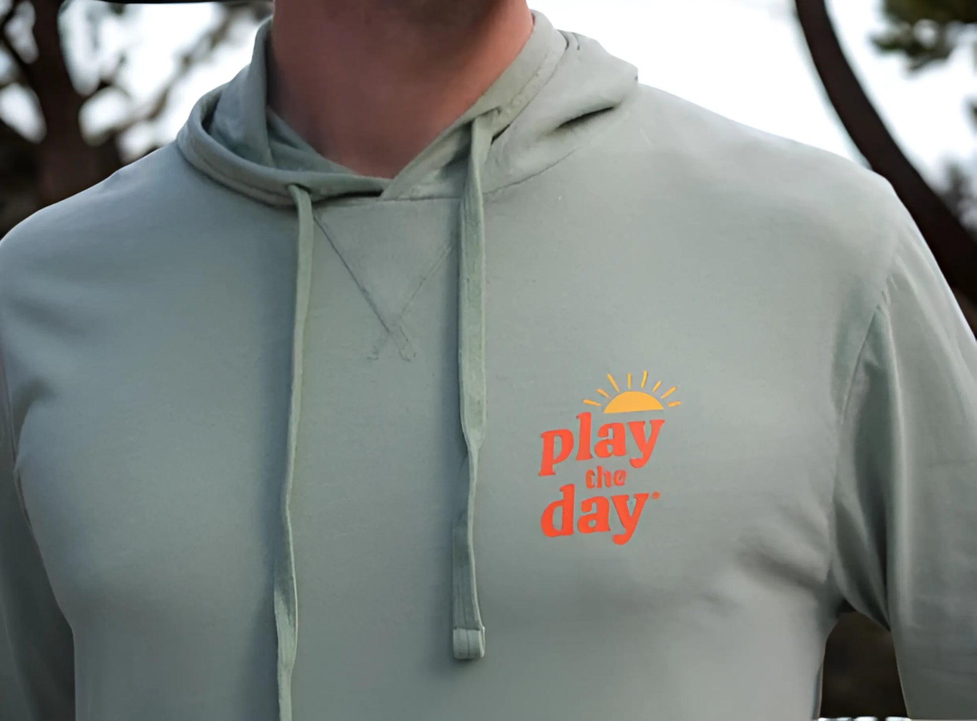 Light green hoodie with 'play the day' text on a blurred outdoor background