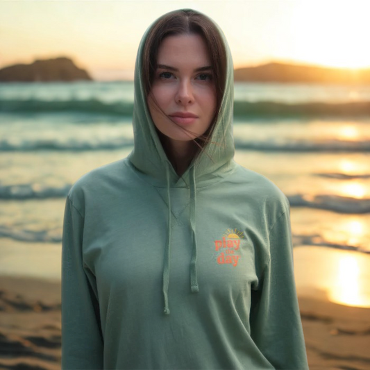Woman wearing a green hoodie with a logo on a beach at sunset