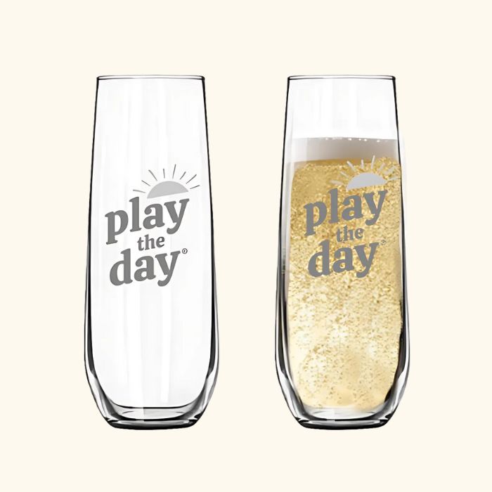 Set of two stemless champagne flutes with deep-etched Play the Day® logo, one shown with bubbly