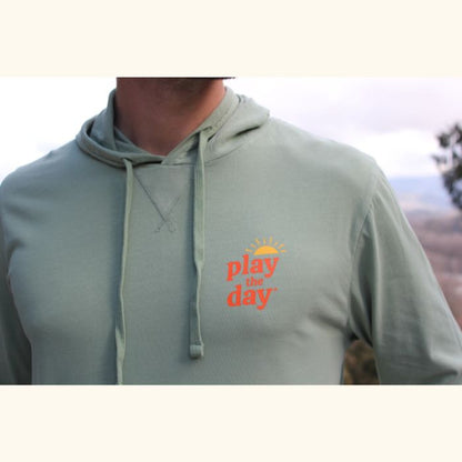 Close-up of Play the Day® logo on green long sleeve hooded tee made from soft cotton-blend fabric