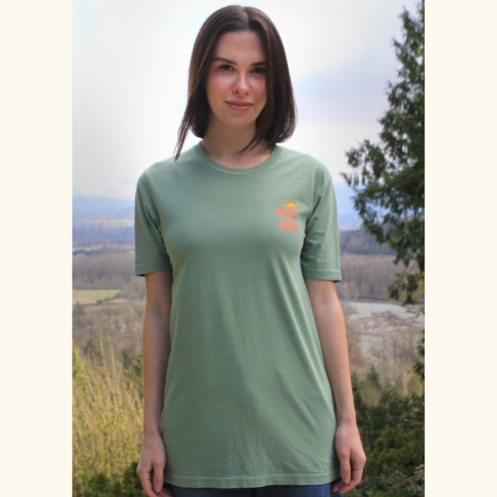 Woman wearing green Play the Day® unisex t-shirt, front view in outdoor setting