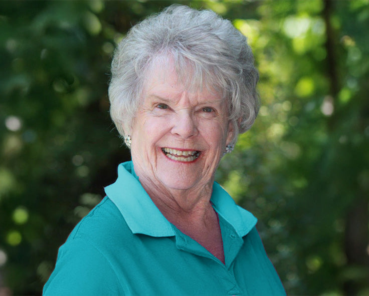 Portrait of Sydney Dickinson smiling in a teal polo shirt, with a forested background.