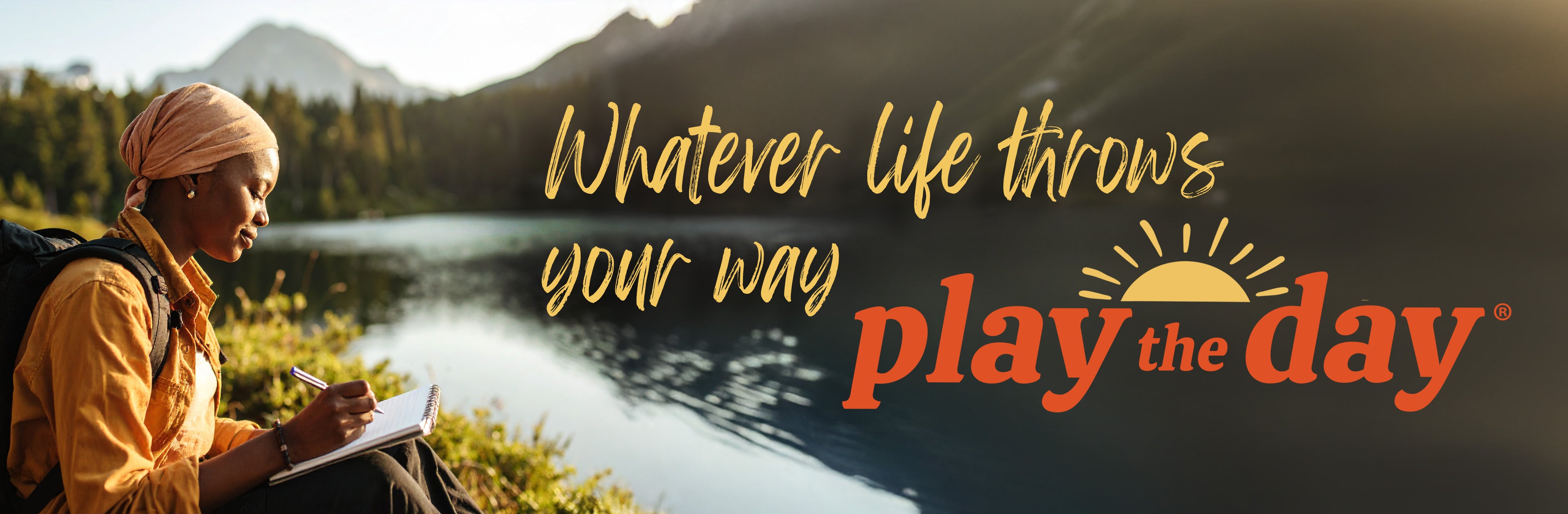 A woman journaling by a mountain lake with the quote ‘Whatever life throws your way, play the day.’ in overlay text.